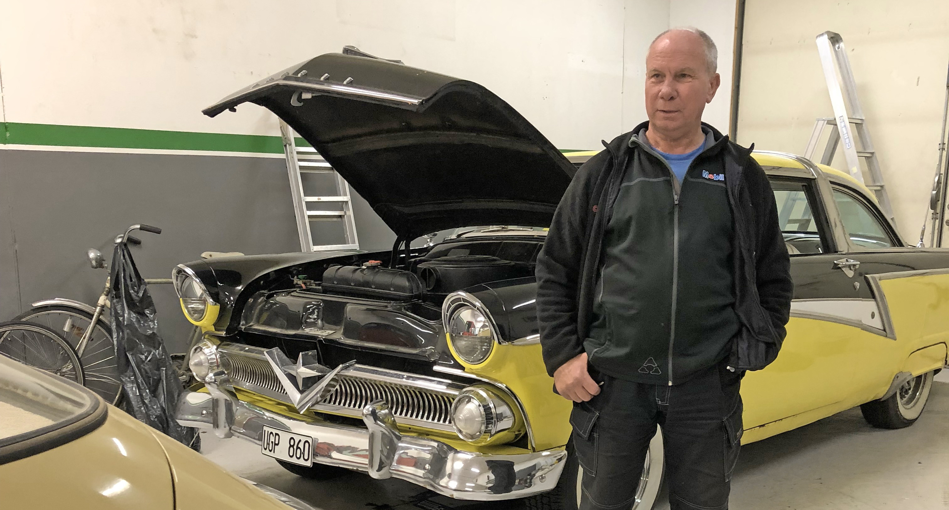 Jerry framför en jänkare i garaget. Motorhuven är öppen. Bilen är gul och svart.